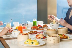 A breakfast buffet with various dishes, including pancakes, omelets, and pastries, served on a marble table.