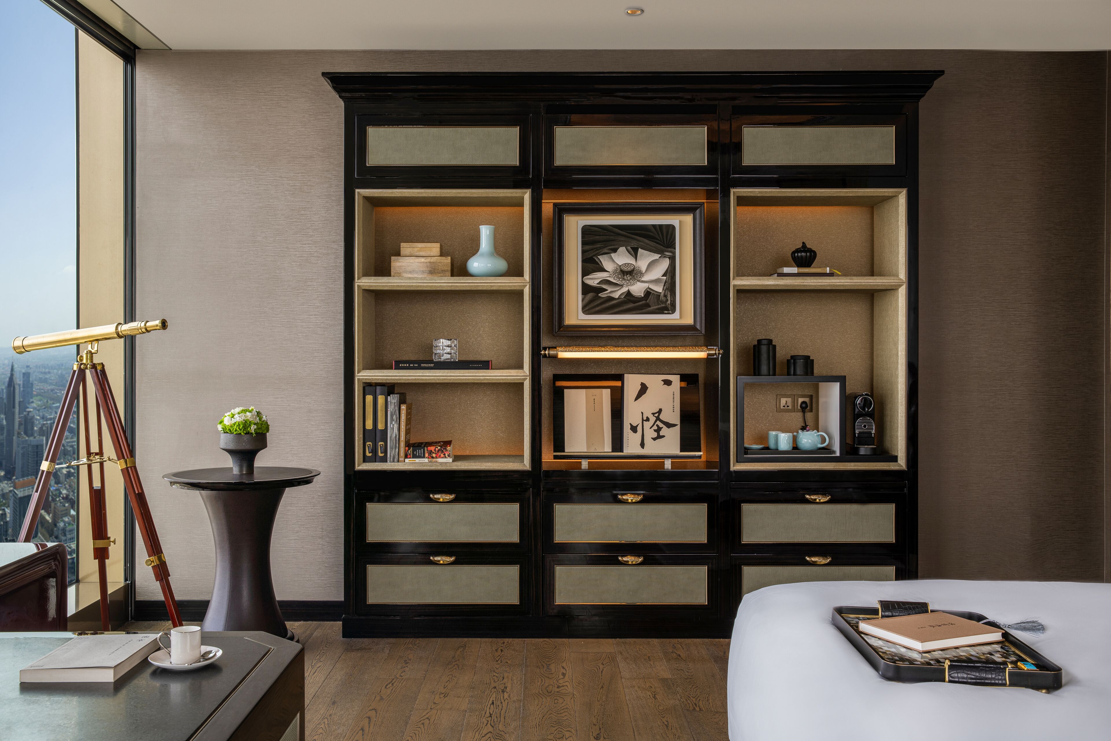 Ein Hotelzimmer mit einem großen Bett, einem Schreibtisch mit Lampe, einem Bücherregal und Blick auf die Stadt.