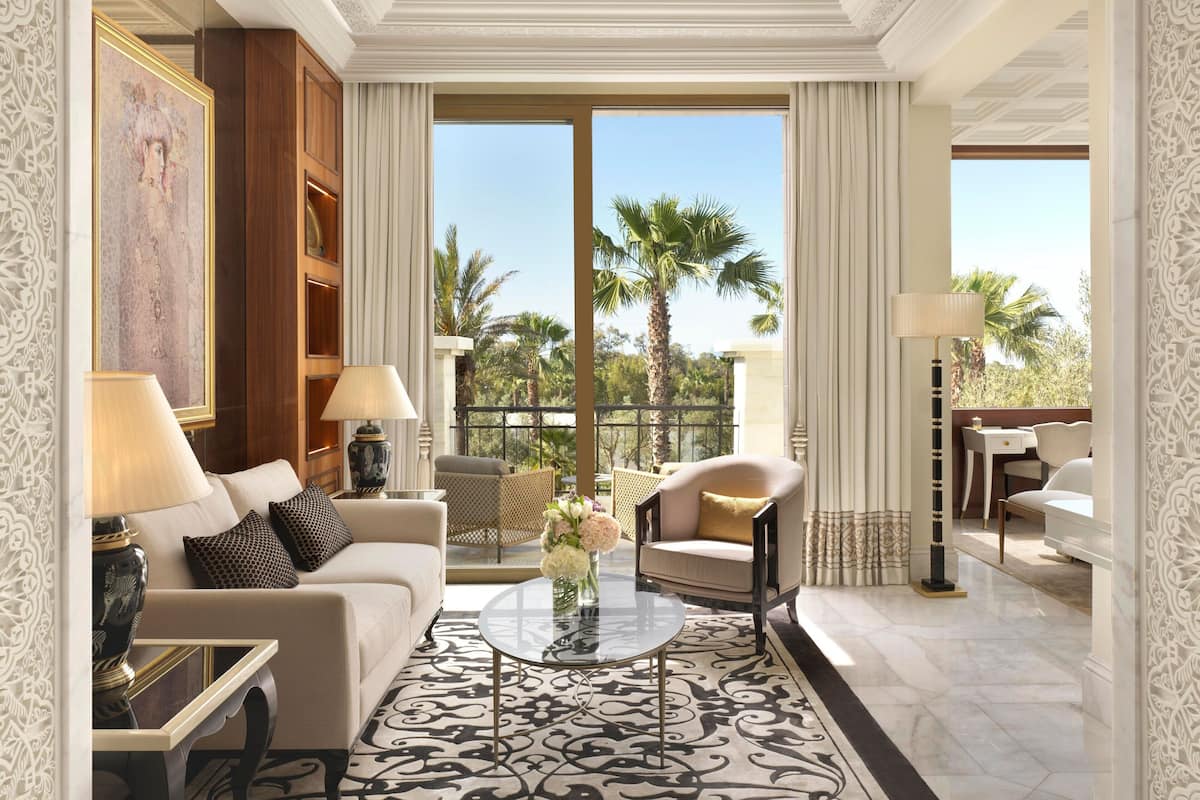 Ein luxuriöses Wohnzimmer mit einer Couch, Sesseln, einem Couchtisch und Blick auf Palmen durch große Fenster.