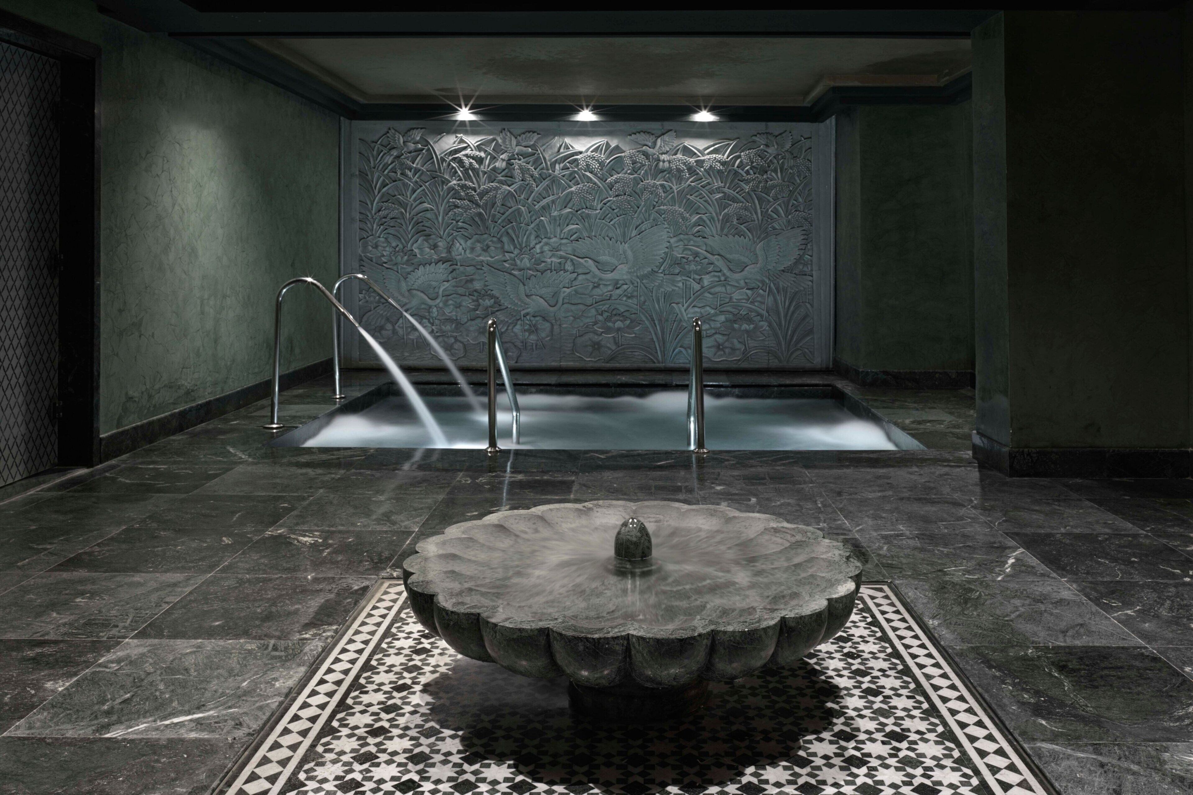 A spa area with a stone fountain, a hot tub, and a wall with floral carvings.