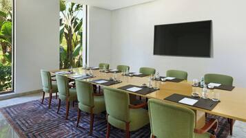 A conference room with a long table, green chairs, and a large screen on the wall.