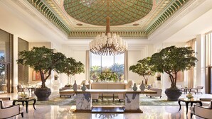 A luxurious lobby with a grand chandelier, a marble reception desk, and two large potted trees. - The Ritz-Carlton Rabat, Dar Es Salam (Rabat)