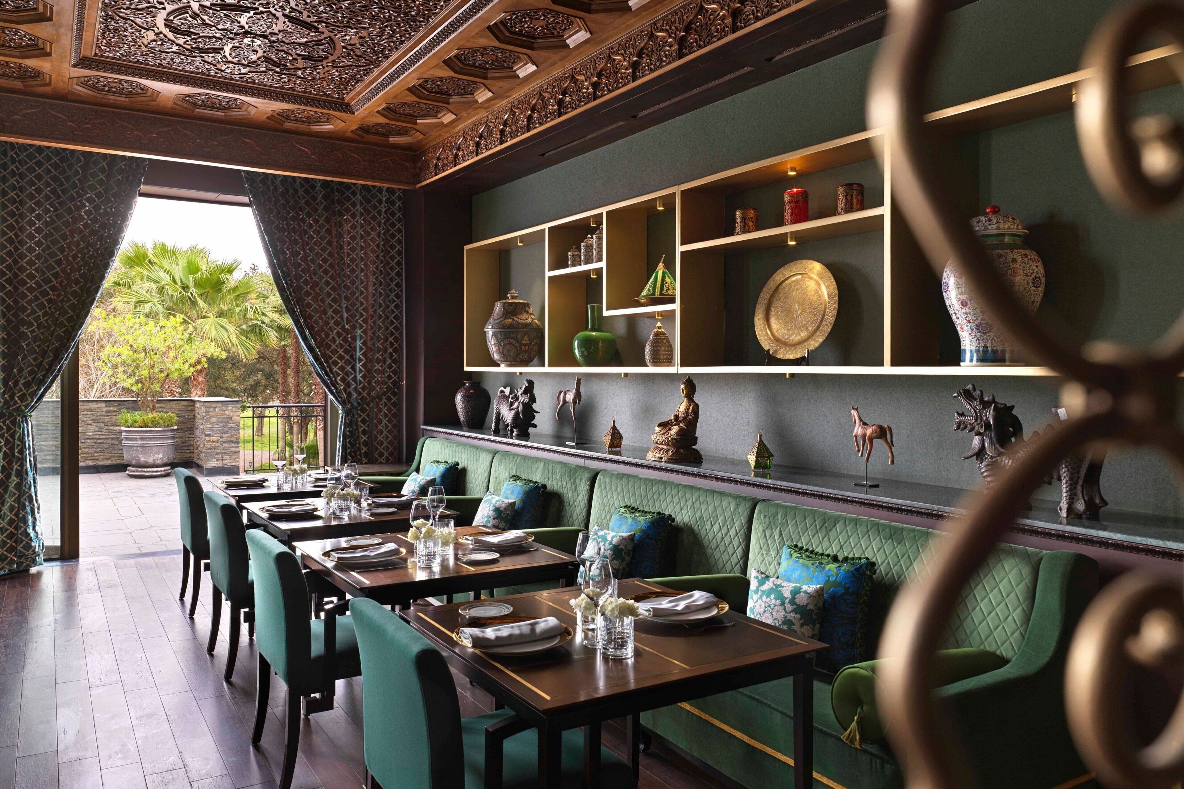 A restaurant with green upholstered booths and a high ceiling with intricate woodwork.