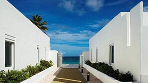 Een pad dat naar een strand leidt, met witte gebouwen en een helderblauwe lucht.
