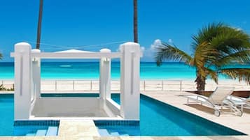 A pool area with a view of the beach, palm trees, and a clear blue sky.