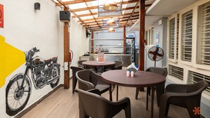 Comedor con mesas y sillas redondas, un mural de una motocicleta y una cocina al fondo.