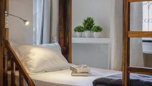 Un dormitorio acogedor con estructura de cama de madera, una lámpara de noche, una planta pequeña en un estante y una pila de libros.