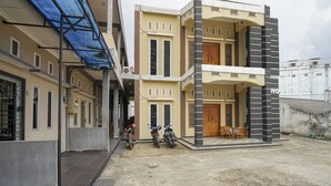 A multi-story residential building with a covered outdoor area, two motorcycles parked outside, and a small seating area with chairs.