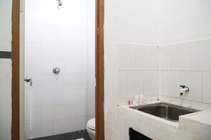 A bathroom with white tiles, a shower, a toilet, and a sink with toiletries. - OYO 1861 Martha Guest House (Balikpapan)