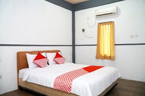 A hotel room with a bed, white walls, a brown headboard, a red and white patterned bedspread, and a window with a yellow curtain. - OYO 1861 Martha Guest House (Balikpapan)