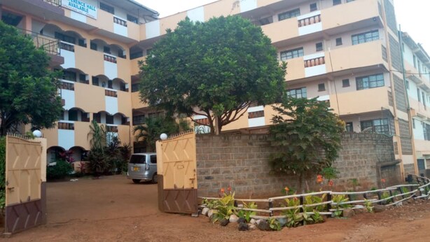 Un edificio de varios pisos con un patio central, un árbol y una entrada protegida por una reja.