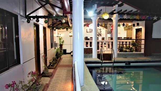 A pool area with a tiled walkway, potted plants, and a pergola with string lights. - Linde's Inn Coron (Coron)