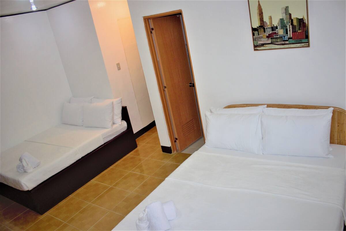 A hotel room with two beds, a wooden door, and a cityscape painting on the wall.