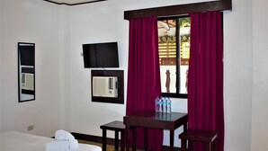 A hotel room with a bed, a table with chairs, a TV, an air conditioner, and a window with curtains. - Linde's Inn Coron (Coron)