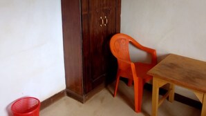 A small room with a wooden cabinet, a red plastic chair, and a wooden table. - Salkan Hotel (Embu)
