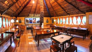 A rustic wooden interior with long tables and benches, a thatched roof, and framed pictures on the walls. - Banjara Camp and Retreat Sangla (Sangla)