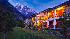 A two-story building with a mountain backdrop, featuring a well-lit entrance and a balcony with a railing. - Banjara Camp and Retreat Sangla (Sangla)