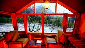 A cozy room with a large window, two chairs, a small table, and a lamp. - Banjara Camp and Retreat Sangla (Sangla)