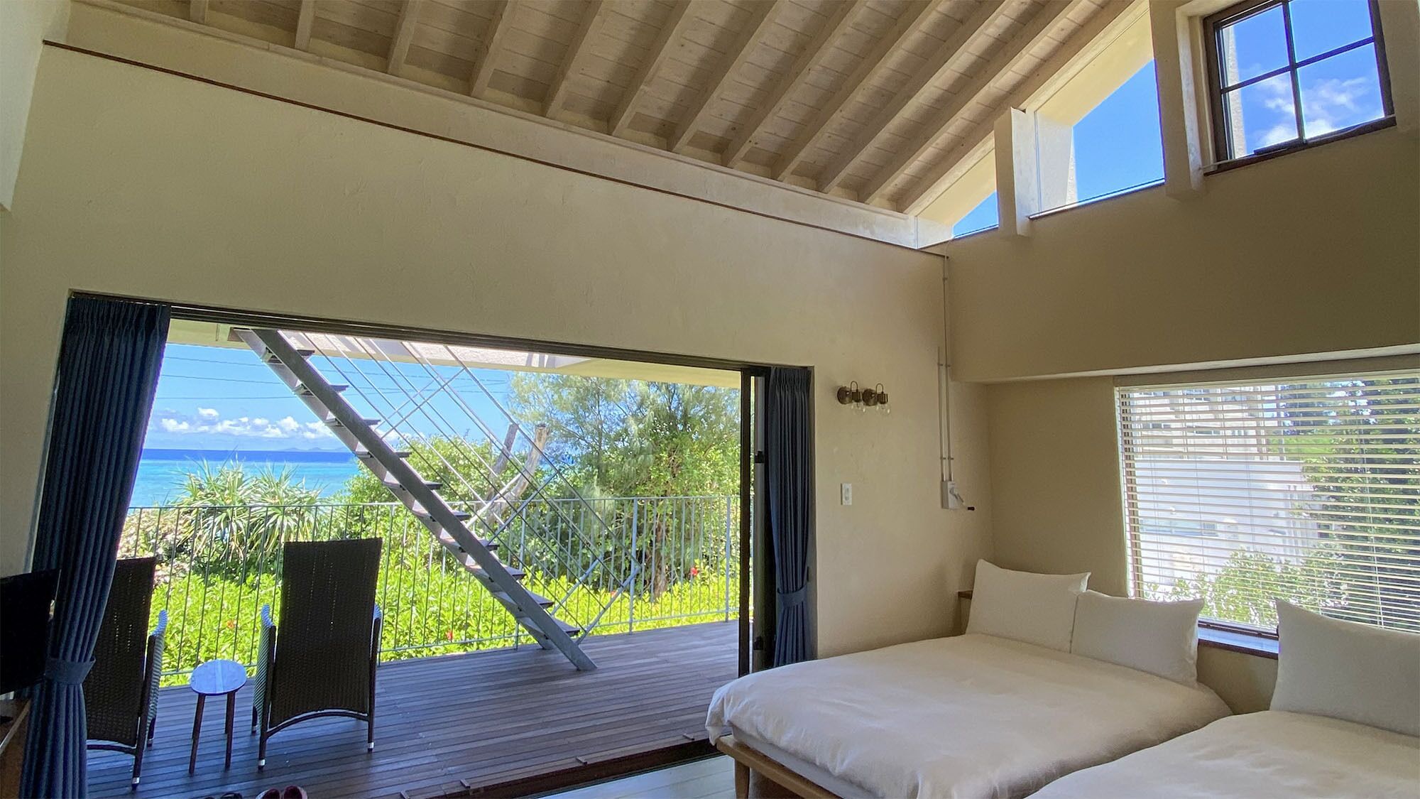 A bedroom with a bed, a chair, a small table, and a view of the ocean through a glass door.