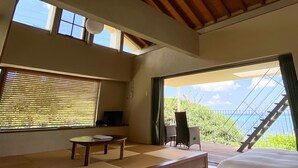 Ein Zimmer mit einem großen Fenster, einem kleinen Tisch, einem Stuhl und einem Bett.