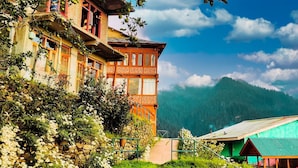 Un bâtiment traditionnel doté d’un balcon, entouré d’une végétation luxuriante et ayant une chaîne de montagnes en toile de fond.