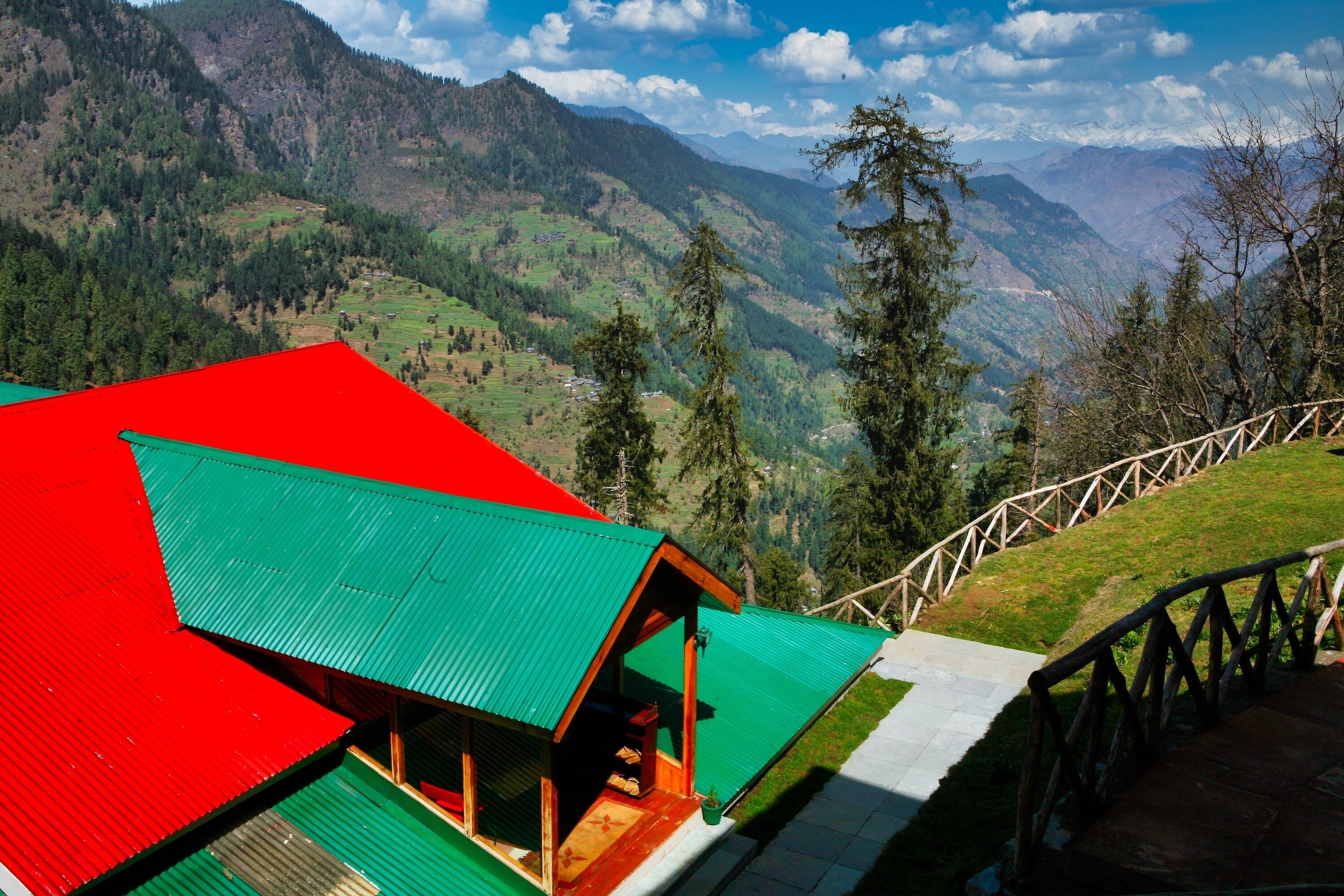 A mountain lodge with a red and green roof, wooden structure, and a view of the surrounding mountains.