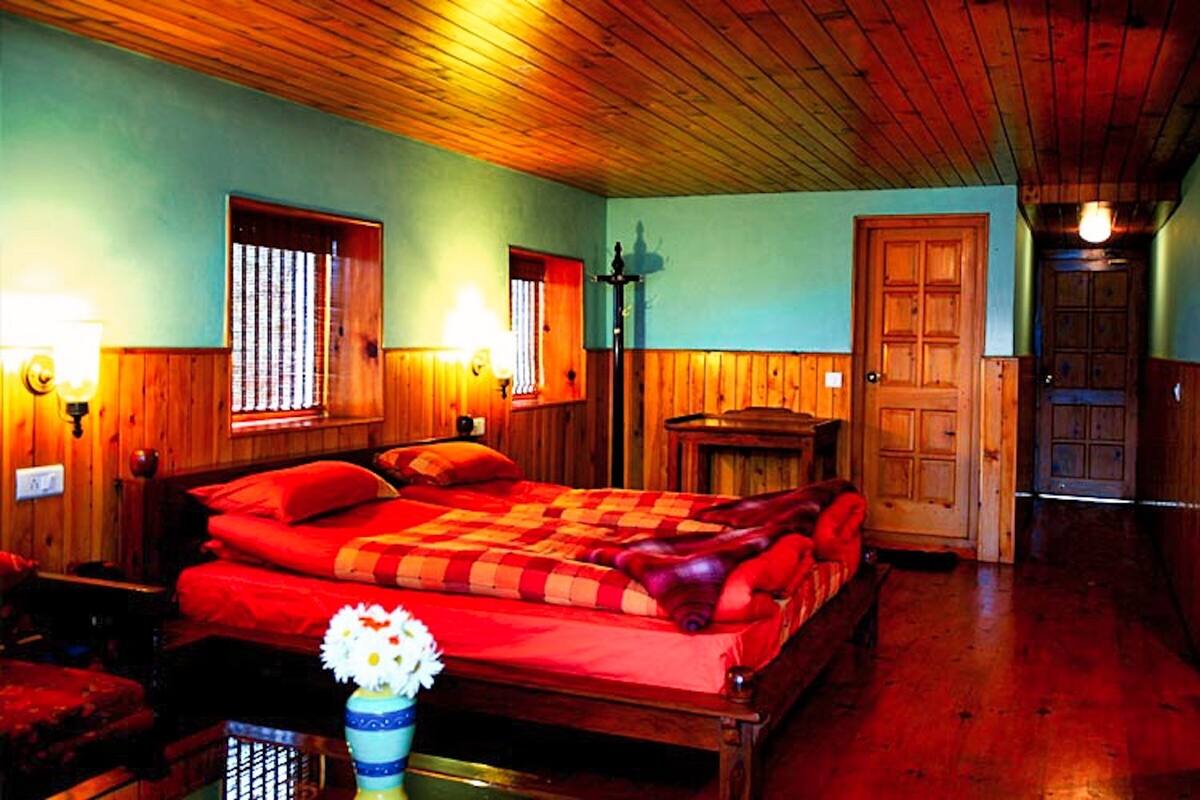 Une pièce avec un plafond en bois, un lit avec une literie rouge, une table de chevet, une lampe fixée au mur et une porte.