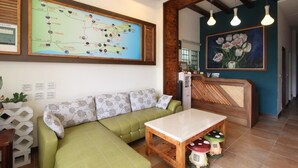 Un área de recepción con un sofá verde, una mesa de madera, un mapa en la pared y un cuadro de flores.