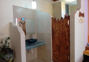 Baño con lavamanos de piedra, cabina de ducha de madera y espejo con luz.