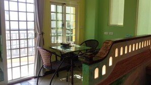 Un comedor con mesa de vidrio y sillas de mimbre, una pared de acento verde y vistas a través de un ventanal.