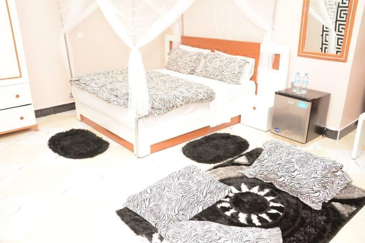 A bed with a canopy, a bedside table with a water bottle, and a small refrigerator.