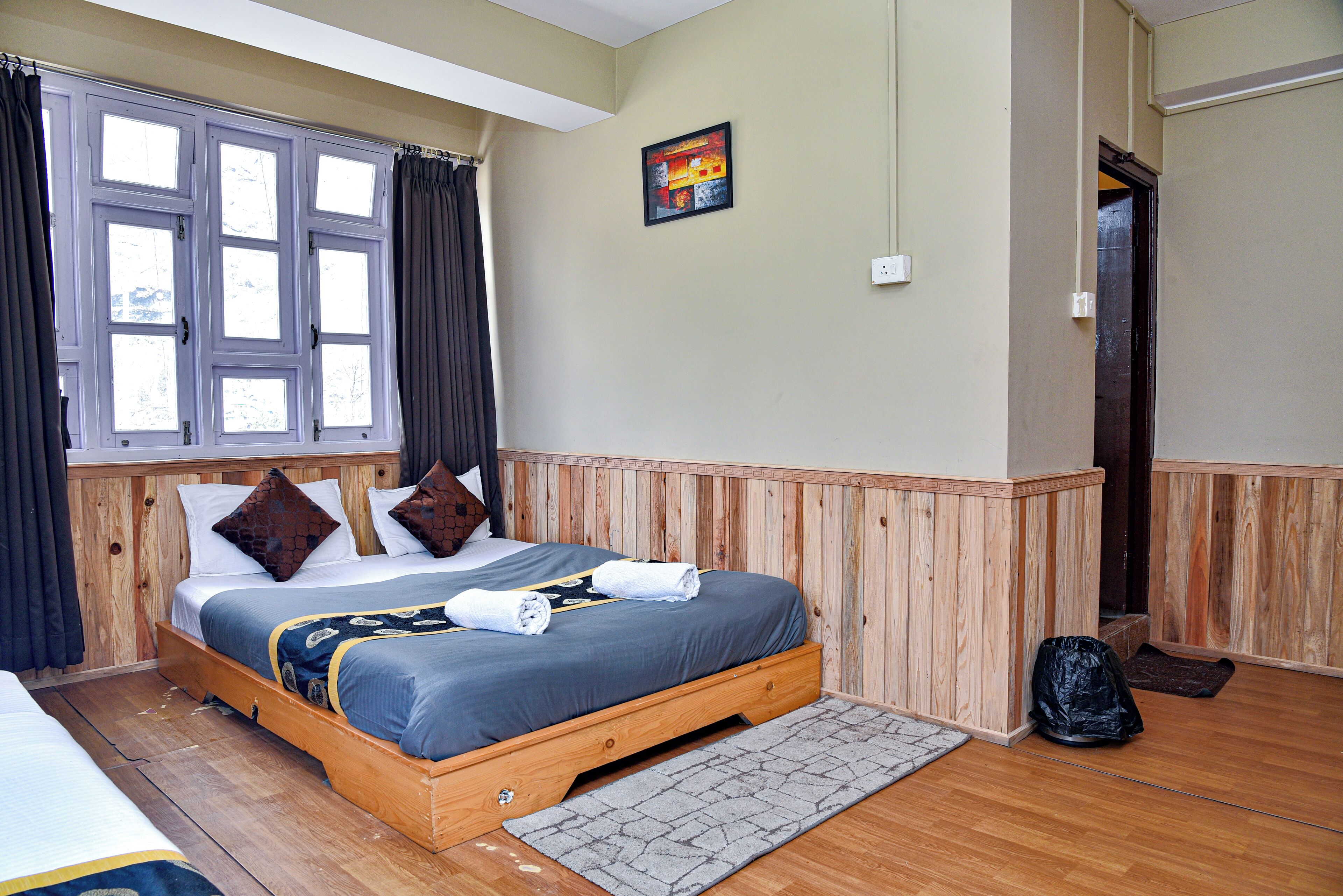 Un dormitorio con cama de madera, una ventana con cortinas, un cuadro en la pared y una puerta.