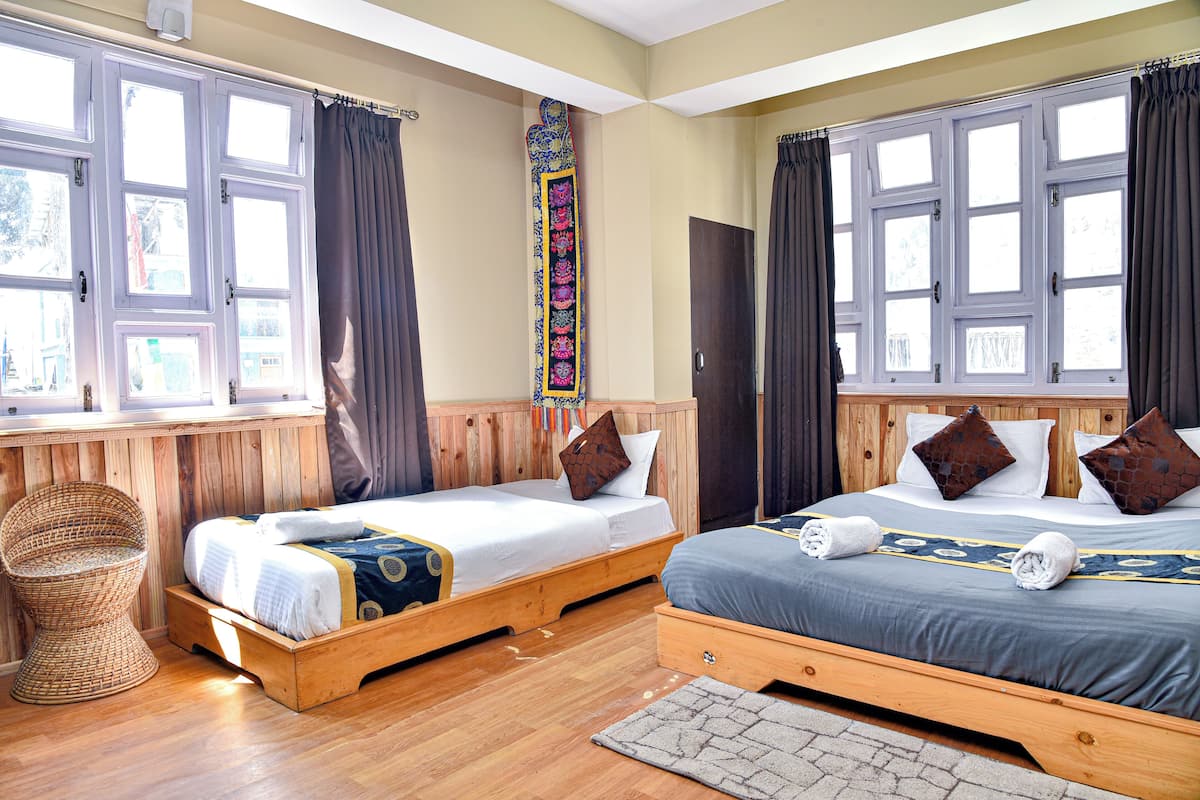 A hotel room with two wooden beds, a woven chair, and large windows with curtains.