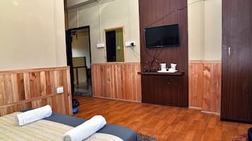 A hotel room with wooden paneling, a bed with towels, a TV mounted on the wall, and a small shelf with toiletries.