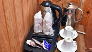 Una estación de café con una cafetera, dos bolsas de papel, un termo y dos tazas sobre una mesa de madera.