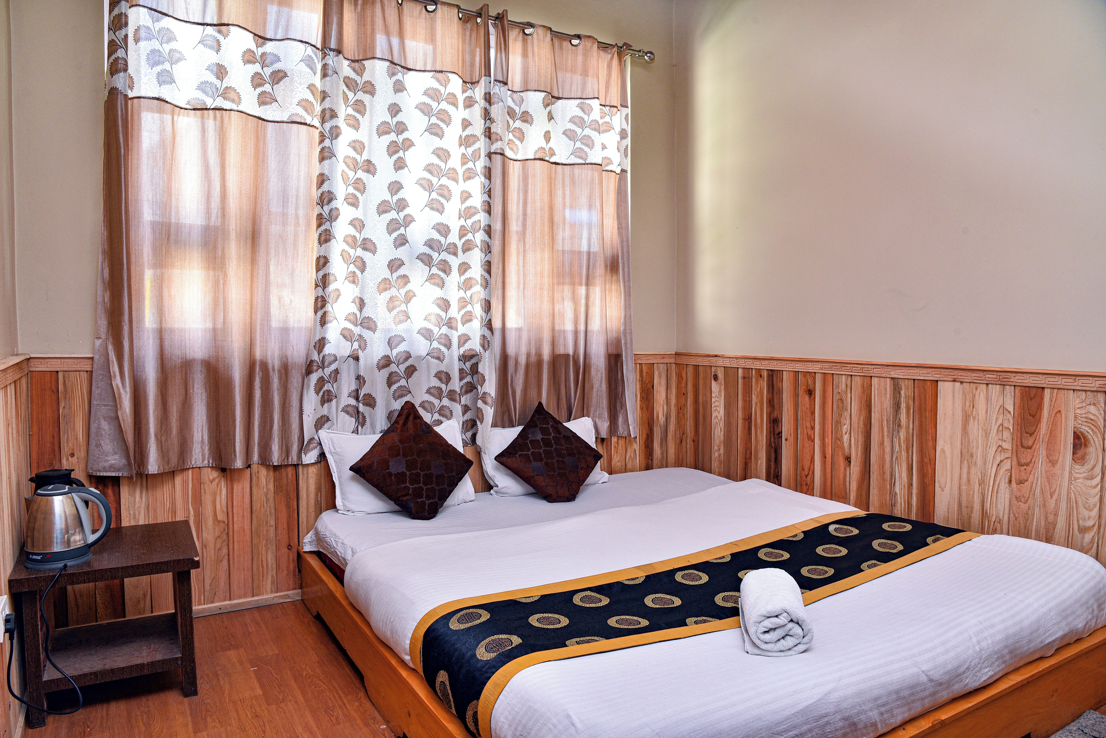 A neatly made bed with a patterned bedspread, two pillows, and a rolled towel on the side.