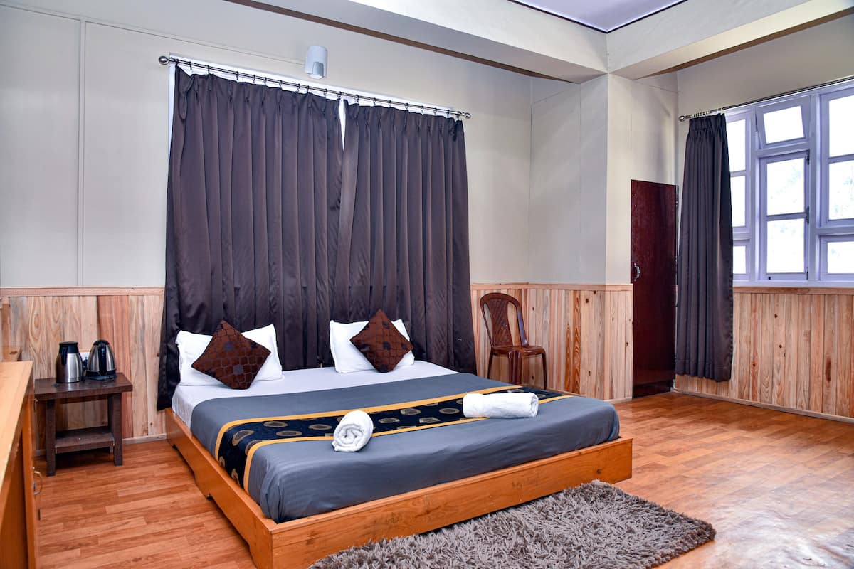 A neatly made bed with a dark headboard, a wooden nightstand with a kettle, and a window with curtains.