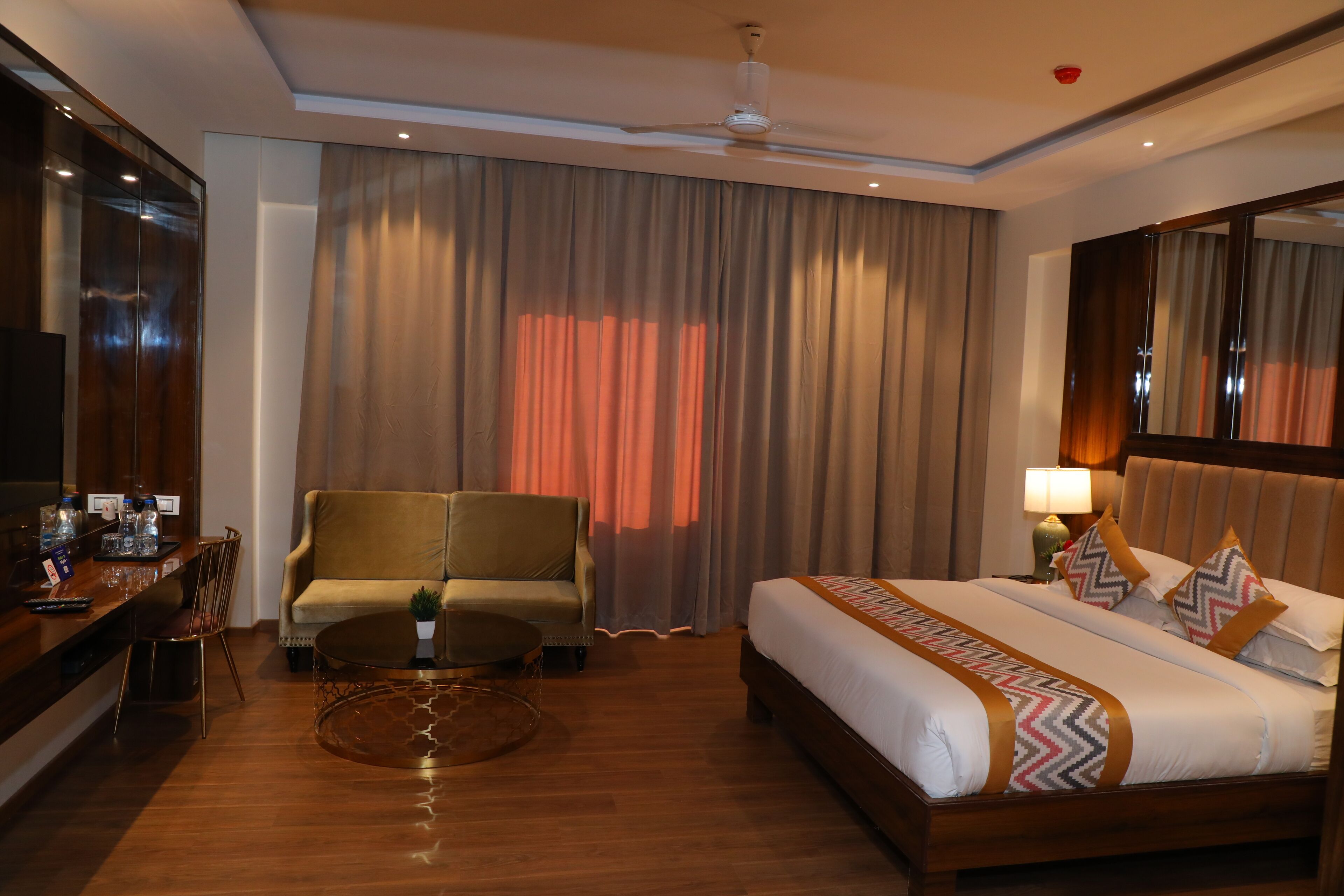 Una habitación de hotel con cama, sofá, una mesita, televisor y espejo.