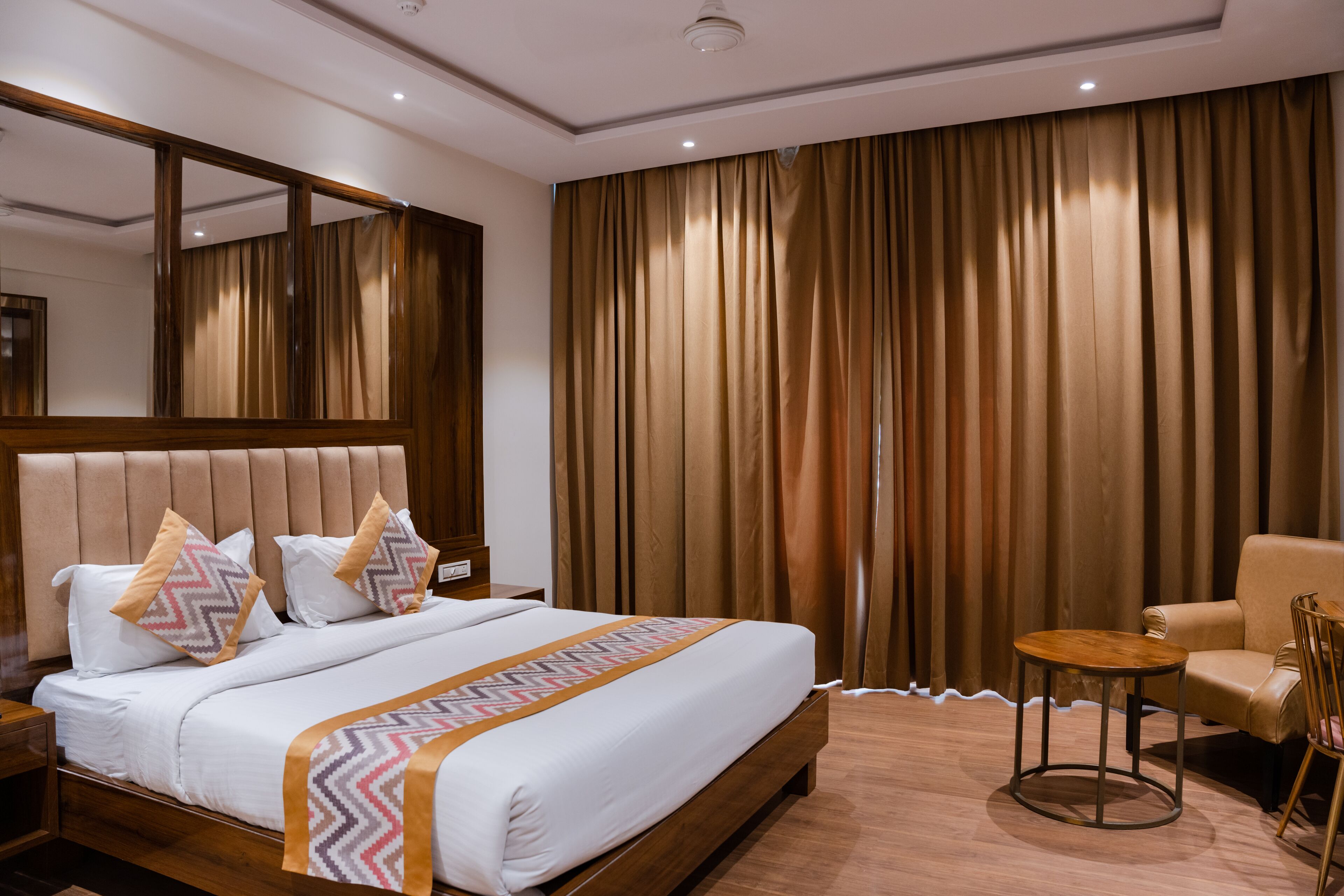 Una habitación de hotel con una cama grande, un cabecero de madera, una mesita redonda pequeña y una silla.