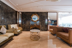 A spacious lobby with marble flooring, two sofas, a round table, and a large mirror. - Oaktree Hotel (Morbi)