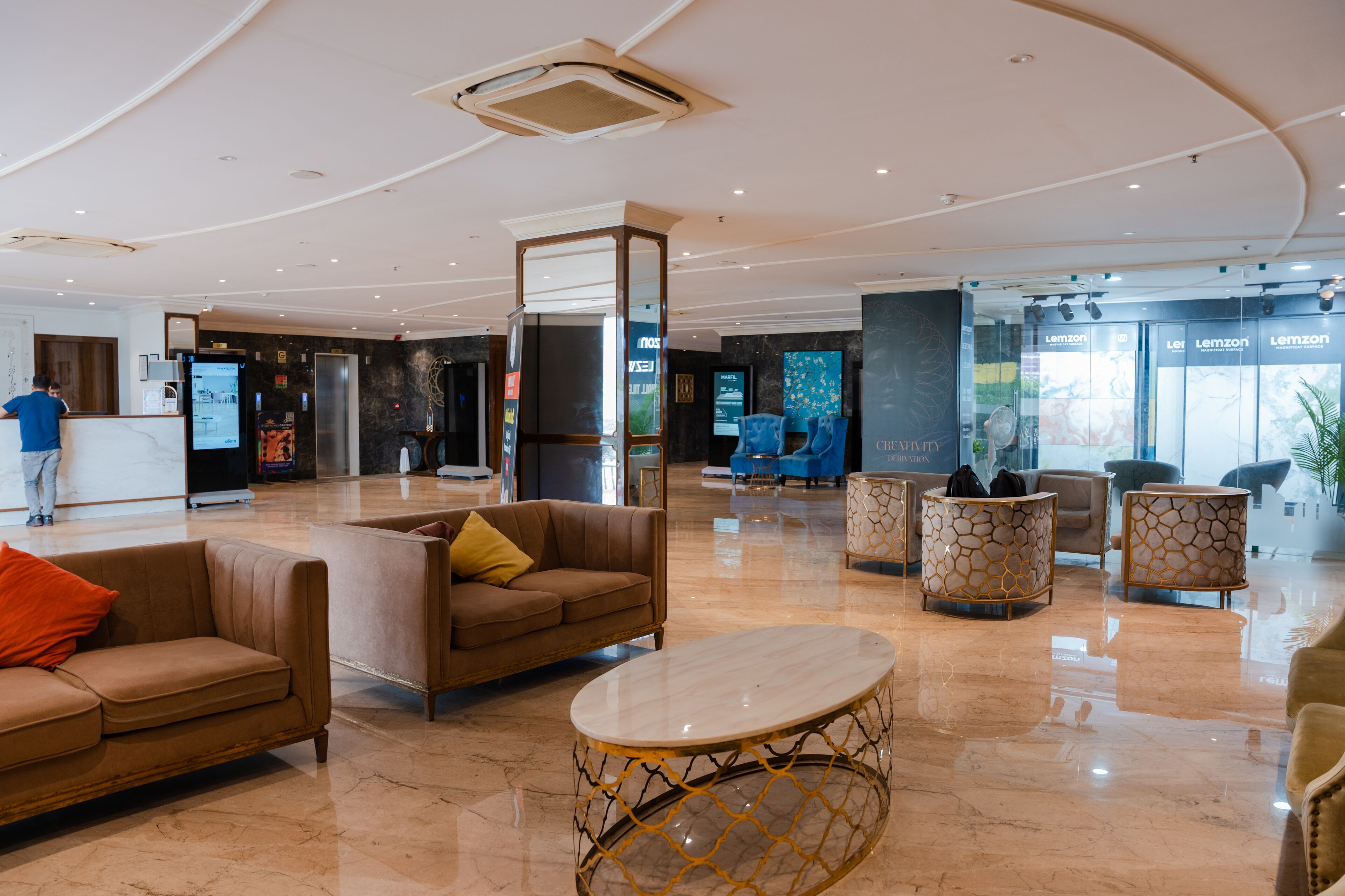 A spacious lobby with a reception desk, seating area with sofas and armchairs, and a polished marble floor.