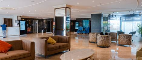 A spacious lobby with a reception desk, seating area with sofas and armchairs, and a polished marble floor.
