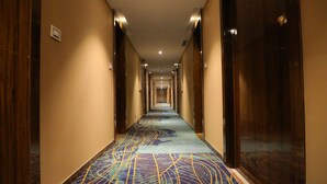 Un lungo e stretto corridoio d'albergo con una moquette decorata e porte di legno su entrambi i lati.