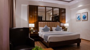 Una camera d'albergo con un letto grande, una testiera in legno, una scrivania con una sedia e due lampade da comodino.