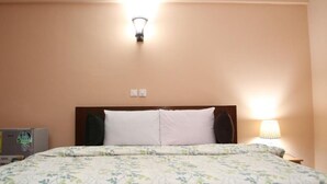 A hotel room with a bed, a nightstand, a lamp, and a wall-mounted light fixture. - Mama Lee's Lodge - Yamoransa (Fomena)