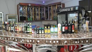 A bar area with a variety of liquor bottles, a Guinness refrigerator, and a selection of snacks and drinks on the counter. - Mama Lee's Lodge - Yamoransa (Fomena)