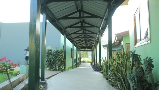 A covered walkway with a tiled floor, flanked by green walls and potted plants. - Mama Lee's Lodge - Yamoransa (Fomena)