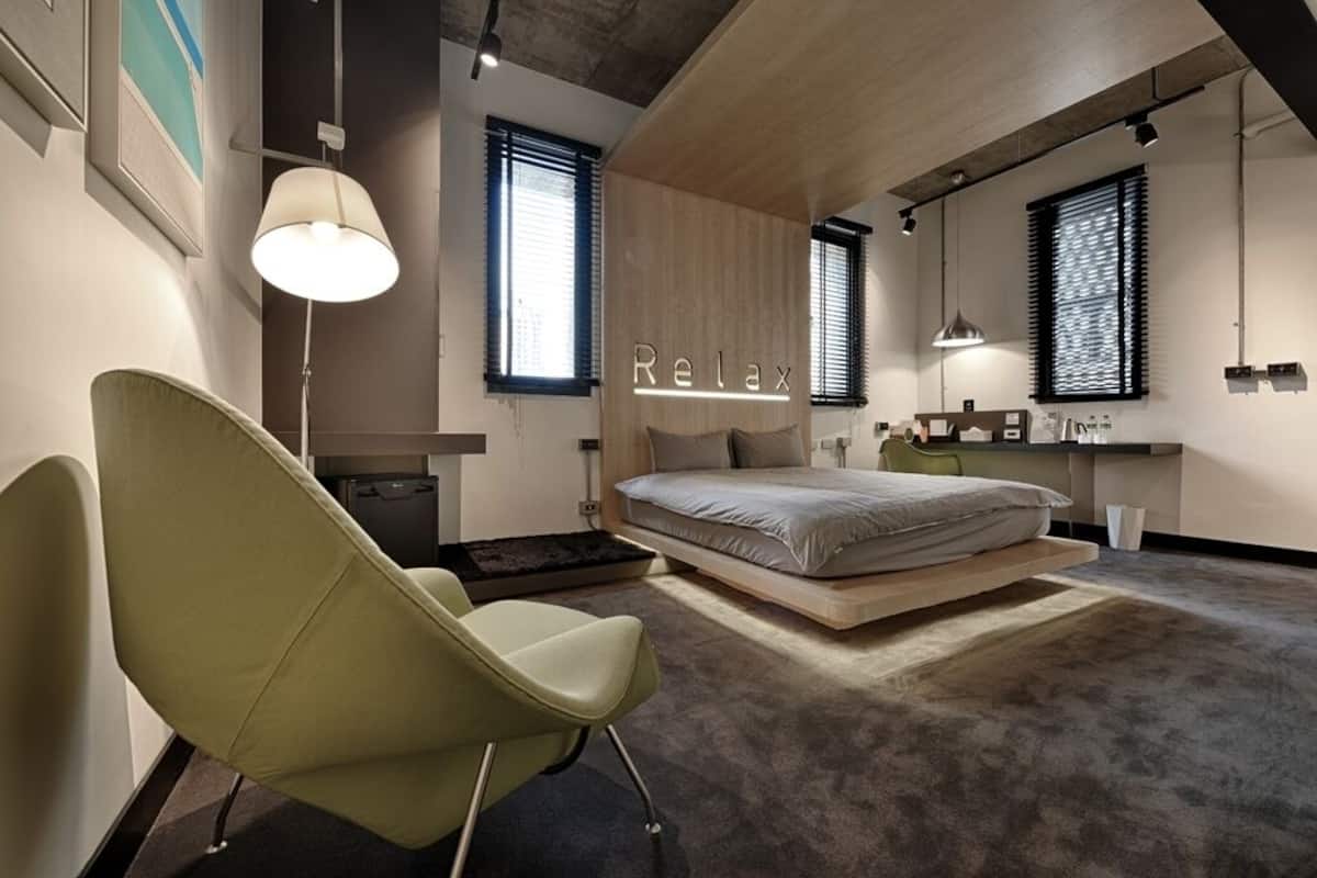 A modern bedroom with a bed, a chair, a desk, and a large window.