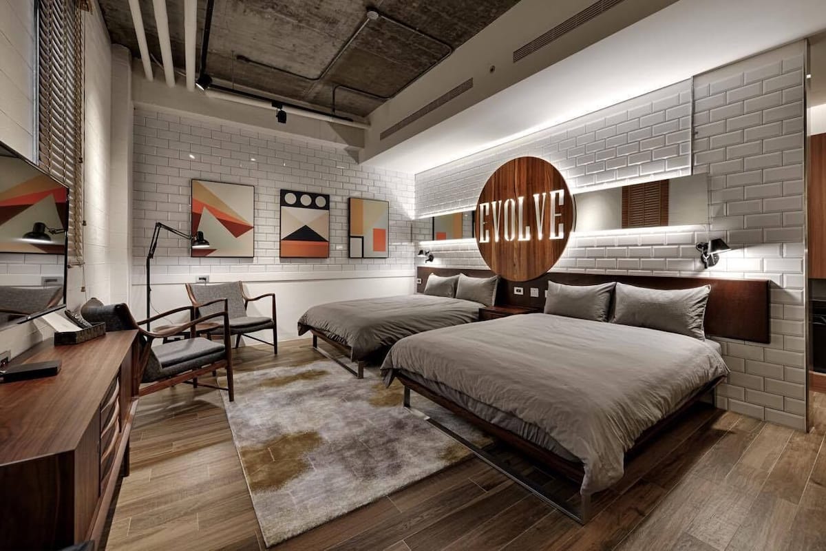 A modern bedroom with two beds, a desk, and a large 'EVOLVE' sign on the wall.