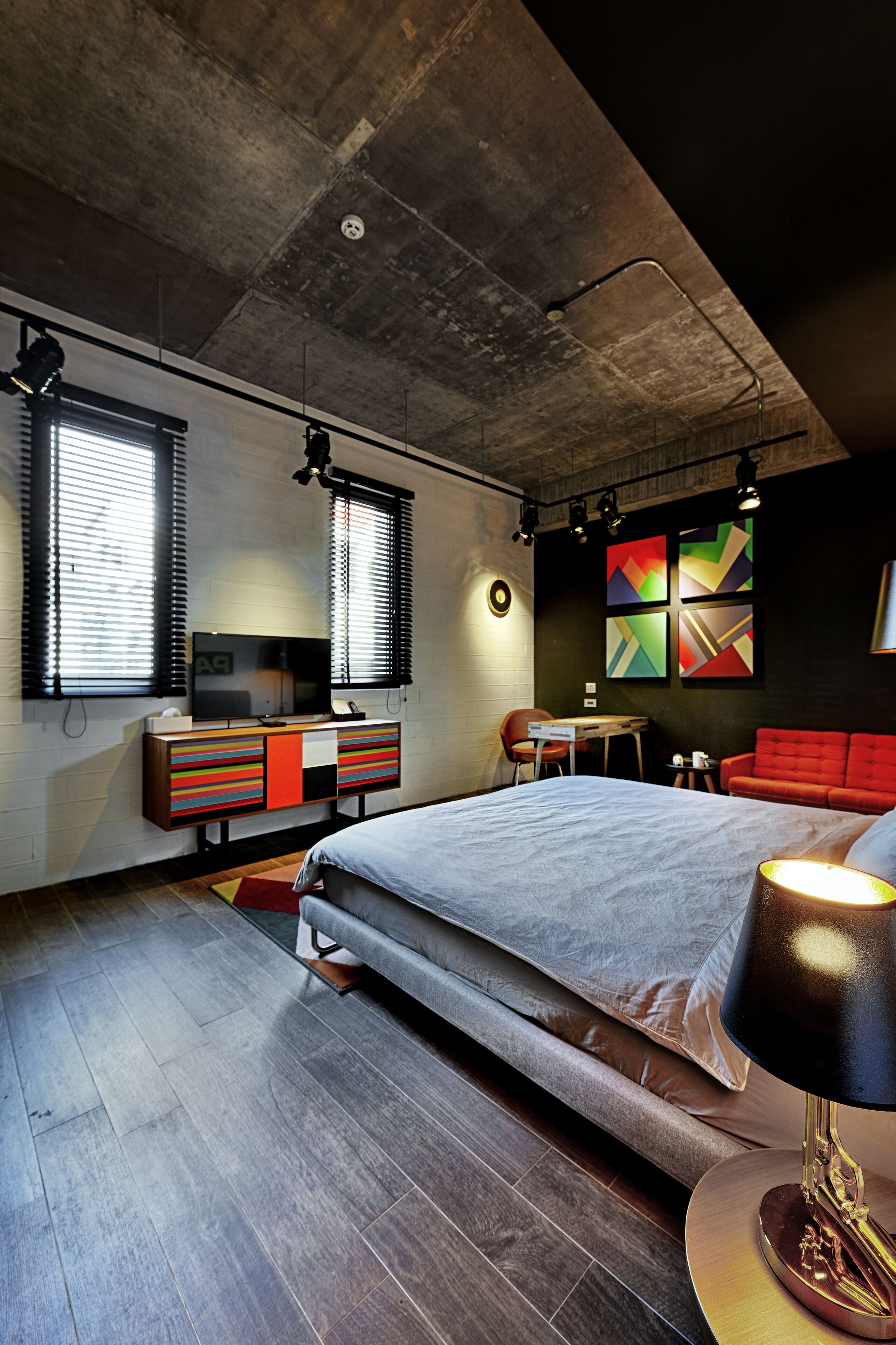 A modern bedroom with a large bed, a desk, a red sofa, and a TV on a wooden dresser.
